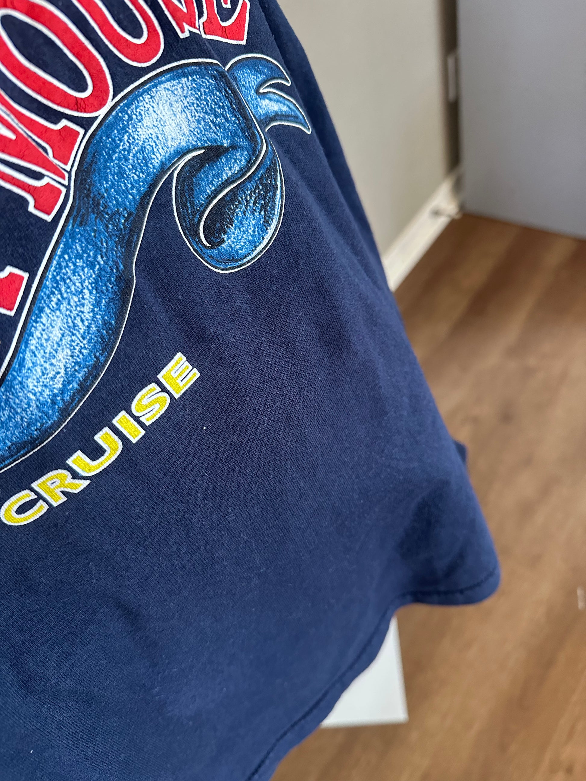 Close-up of a navy blue vintage graphic t-shirt featuring a blue snake design and yellow 'CRUISE' text, with a blurred indoor room background.