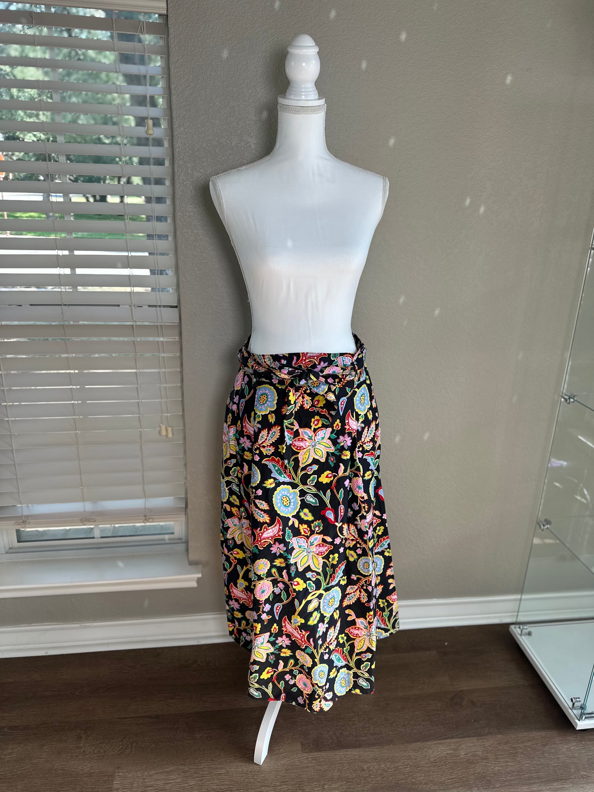 A black midi skirt with a vibrant multicolor floral print, displayed on a white dress form mannequin in an indoor room setting.